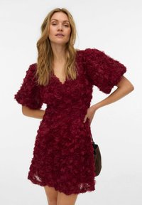 Bordowa sukienka z trójwymiarowymi różami, głębokim dekoltem w serek i bufiastymi rękawami. Wykonana z teksturowanej tkaniny, o luźnym kroju i długości do ponad kolan.