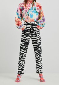 Suéter floral multicolor con cuello alto y mangas voluminosas combinado con pantalones de estampado cebra en blanco y negro y zapatos coloridos con patrones.