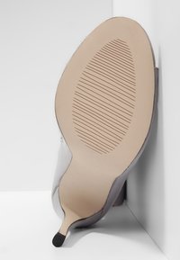 Kengät kirkkaalla korolla, joissa on sileä, kiiltävä päällinen, ohut stiletto-korko ja teksturoitu beige pohja, jossa on pystysuorat urat pidon parantamiseksi.