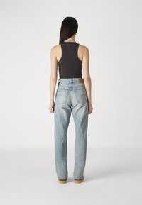 Svetlomodré džínsy s vysokým pásom a rovnými nohavicami, s vreckom na zadnej strane a jemnými detailmi šitia. V kombinácii s priliehavým čiernym tielkom.
