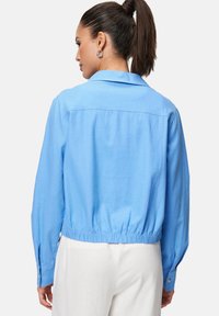 Veste courte bleu clair avec une taille ceinturée, des manches longues et des accents de boutons. Texture lisse et détail de col classique au dos.