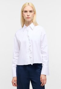 Camicia bianca a maniche lunghe con un bavero arricciato e colletto strutturato, realizzata in tessuto liscio con un design cropped.