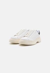 Hvite sneakers med en teksturert læroverdel, med kontrasterende svart hæl, rund tå, tykk gummisåle og snøring.