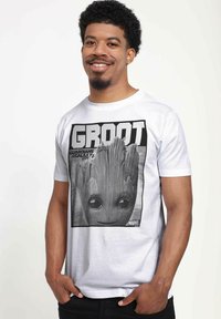 Bílý bavlněný tričko s černobílou grafikou Groota z Strážců galaxie, s velkýma očima a texturovanými dřevitými detaily.
