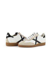 White leather sneakers with black accents. Suede detailing, flat laces, and gum rubber sole. Simple design with a contrasting cross pattern.