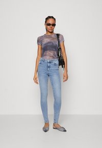 Gjennomsiktig grå tie-dye t-skjorte, høyt liv lys blå skinny jeans, grå lavt helte sko med spiss tupp, og en liten svart håndveske.