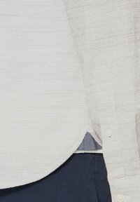 Witte, textuurachtige shirt met horizontale strepen, voorzien van een gebogen zoom en knopen. Draagt over donkerblauwe broeken.