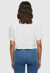 Hvid kortærmet t-shirt, parret med blå højtaljede jeans med baglommer og subtile syningsdetaljer.