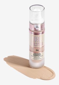 Transparent flaske med pumpe, som inneholder beige foundation. Etiketten har rosa og sølv tekst. Foundation er samlet på overflaten. 23 ml.