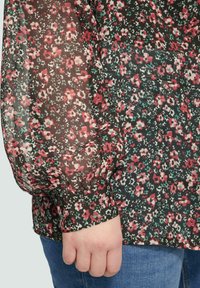 Bluse mit floralem Muster aus durchscheinendem schwarzem Stoff, ausgestattet mit roten, rosa und grünen Blumen. Puffärmel und ein taillierter Bund mit floralem Musterdetail.