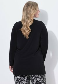 Schwarzes Langarmoberteil mit lockerer Passform, das eine glatte Textur aufweist. Kombiniert mit gemusterten schwarz-weißen Leggings, die Blattmotive zeigen.