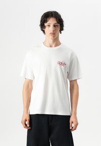 Witte katoen t-shirt met korte mouwen, voorzien van een klein rood grafisch ontwerp op de linkerborst. Eenvoudige, relaxte pasvorm.