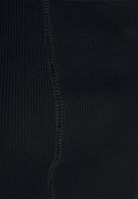 Tecido preto com nervuras, apresentando uma textura suave e costuras visíveis ao longo das emendas, enfatizando um design ajustado e flexibilidade.