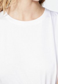 Bílý bavlněný tričko s kulatým výstřihem a krátkými rukávy. Hladký povrch s jednoduchým designem, bez viditelných vzorů nebo akcentů.