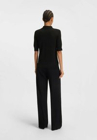 Polo shirt corto nero a maniche corte realizzato in tessuto morbido, abbinato a pantaloni neri aderenti. La parte posteriore presenta un design semplice senza decorazioni.