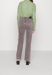 Graue Jeans aus Denim mit geradem Bein, sichtbaren Nähten und zwei Gesäßtaschen. Kombiniert mit einem strukturierten grünen Pullover und Schuhen mit Blockabsatz.