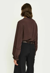 Brun långärmad blus med avslappnad passform, ribbade ärmslut och detaljerad sömnad. Matchad med svarta hög midja-byxor.