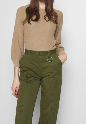 Beige knitted sweater with long sleeves paired with olive green cargo pants featuring a circular silver metal ring at the waistband.