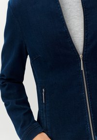 Närbild av en person som bär en mörkblå zip-ups jacka över en ljusgrå ribbad turtleneck-tröja.