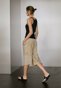 Černý bezrukávový top, béžové culottes s kapsami a černé nazouvací sandály. Hladká textilie s volným střihem, zobrazeno v profilu.
