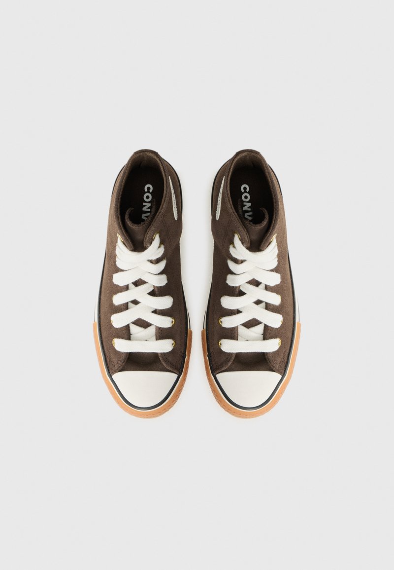 Une paire de baskets montantes en toile brune avec des lacets blancs et des coques en caoutchouc, vues de dessus sur un fond uni.