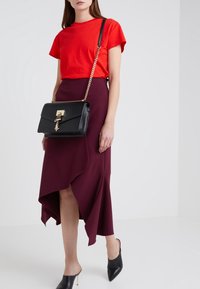 T-shirt rosso a maniche corte, gonna asimmetrica borgogna con rouches, borsa strutturata nera con hardware dorato e mule nere con tacco alto.