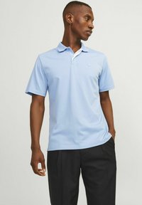 Világoskék pólóing fehér gallérral, rövid ujjakkal és egy diszkrét logóval a mellrészen. Simaságú pamut anyag, laza szabású.