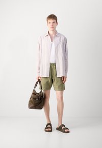 Svītrains, pogājams krekls gaiši rozā un baltā krāsā; balta topa; olīvzaļi šorti; brūna rokassoma; melni sandales. Minimalistisks stils.