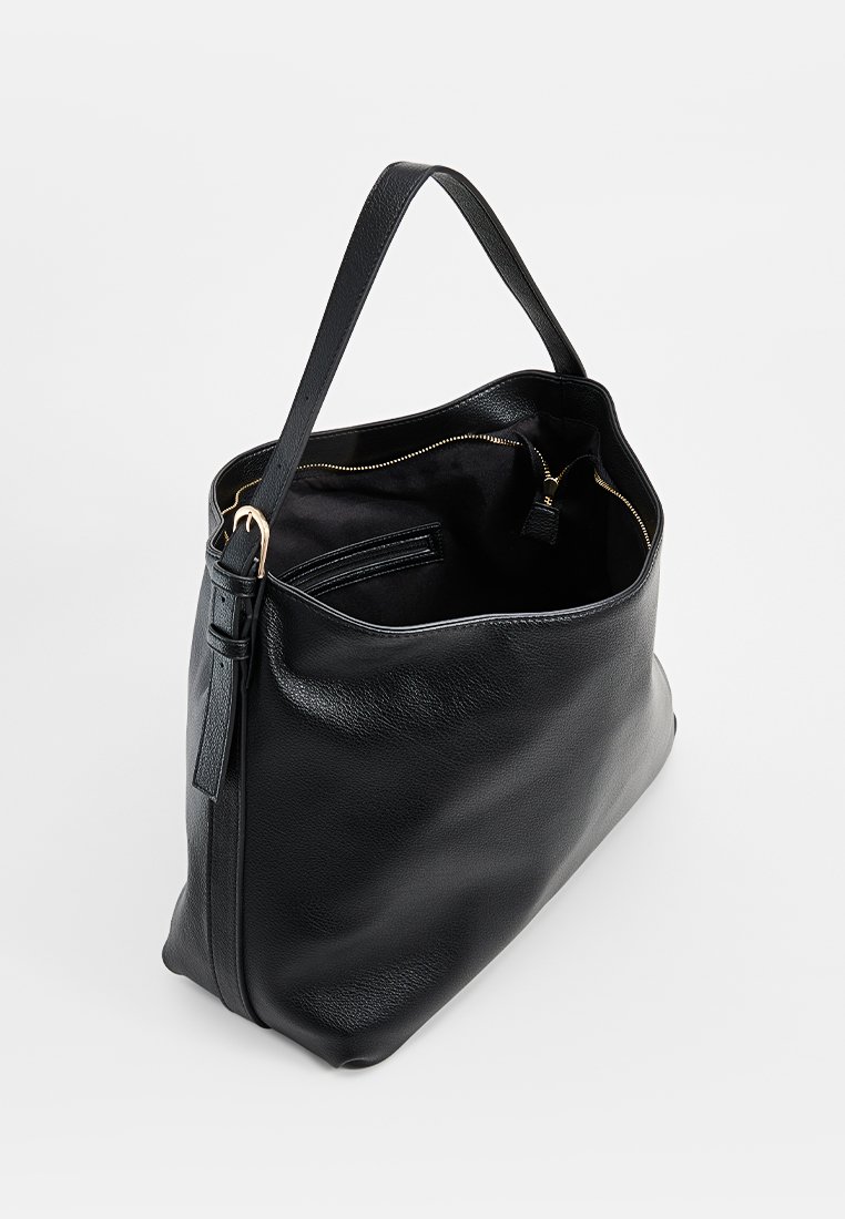Sac fourre-tout en cuir noir avec une texture lisse, sans fermeture sur le dessus et une seule poignée. L'intérieur comporte une poche zippée et un revêtement en tissu.