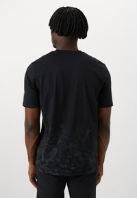 Camiseta negra, de tela de algodón, cuello redondo, mangas cortas, presenta un patrón de camuflaje sutil en la parte baja de la espalda, textura suave.