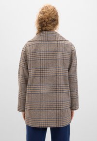 Brun rutig kappa med en avslappnad passform, bred krage och långa ärmar. Har en blandning av beige, orange och marinblå linjer i en texturerad väv.