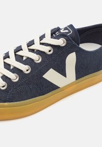 Denim sneakers featuring a navy blue upper with a textured finish, cream laces, and a large white logo on the side. Gum rubber outsole.