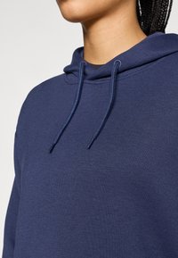 Felpa con cappuccio blu navy realizzata in tessuto morbido, con tasca a marsupio e cappuccio con coulisse. Texture liscia con dettagli di cuciture minimi.