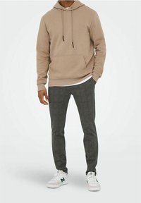 Beige hoodie met trekkoorden en een voorzak, gecombineerd met donkergrijze geruite tapered broek en witte sneakers met groene accenten.