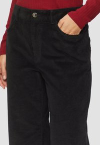 Zwarte corduroy broek met een ribbelstructuur, voorzien van een voorkant pocket, metalen knoopsluiting en een aangesloten taille. Geen zichtbare patronen.