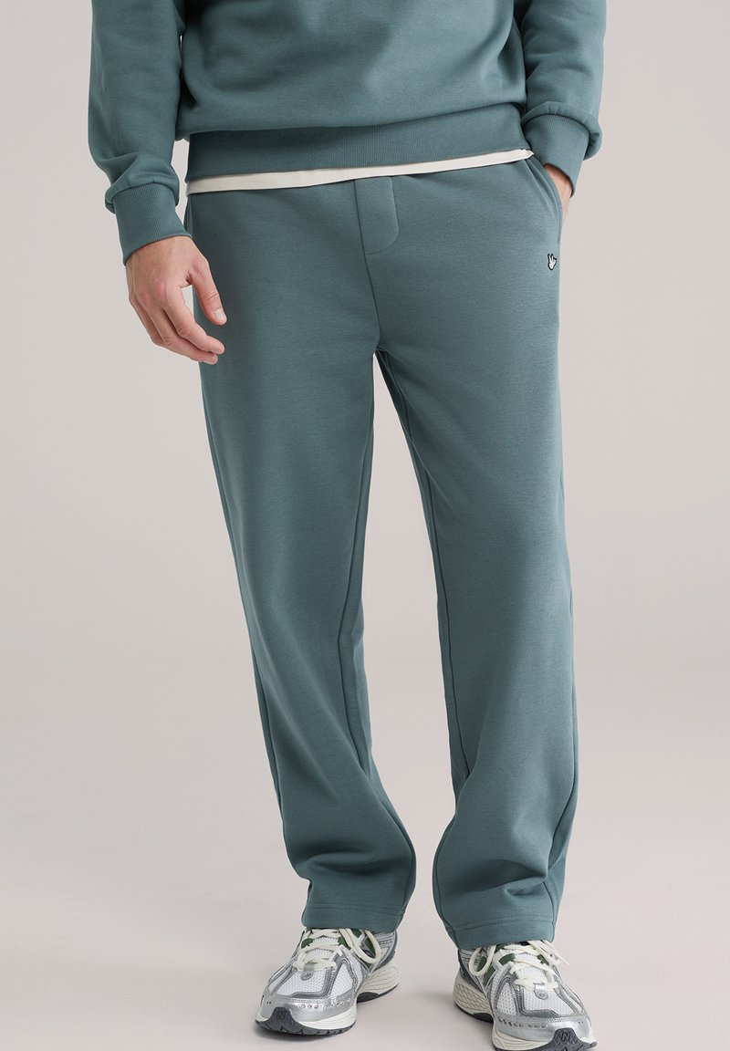 Opustene hlače jogging kroja od tirkiznog materijala sa glatkom teksturom. Imaju prednji džep, elastični pojas i suptilni logotip.