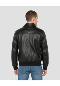 Schwarze Lederjacke mit glatter Textur, klassischem Kragen und gerippten Bündchen, kombiniert mit blauer Jeans. Rückansicht zeigt Nähte und Formgebung.