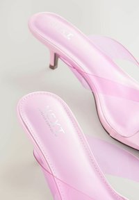 Rozā slaidu apavi ar caurspīdīgām siksnām, gluda satīna tekstūra, šaurs stiletto papēdis un zīmola iekšējā dizaina elementi.