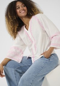 Camicia bianca con ricami rosa lungo le maniche e il davanti, abbinata a jeans a gamba larga blu chiaro, caratterizzati da un fit rilassato e da una trama morbida.
