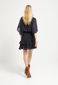 Mörkblå chiffongklänning med ett lager av volang nederkant, lösa ärmar och elastisk midja. Matchad med bruna fransade ankellånga stövlar.