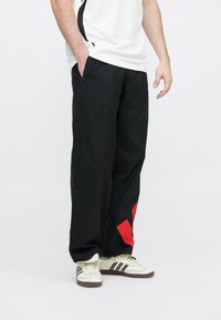 Čierne nohavice z ľahkej tkaniny s veľkým červeným geometrickým zdobením na ľavom diele, s bočnými vreckami a pohodlným strihom.