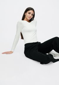 Λευκή μπλούζα με μακριά μανίκια συνδυασμένη με μαύρη φόρμα, με άνετη εφαρμογή και ελαστική μέση. Ομαλή υφή υφάσματος.