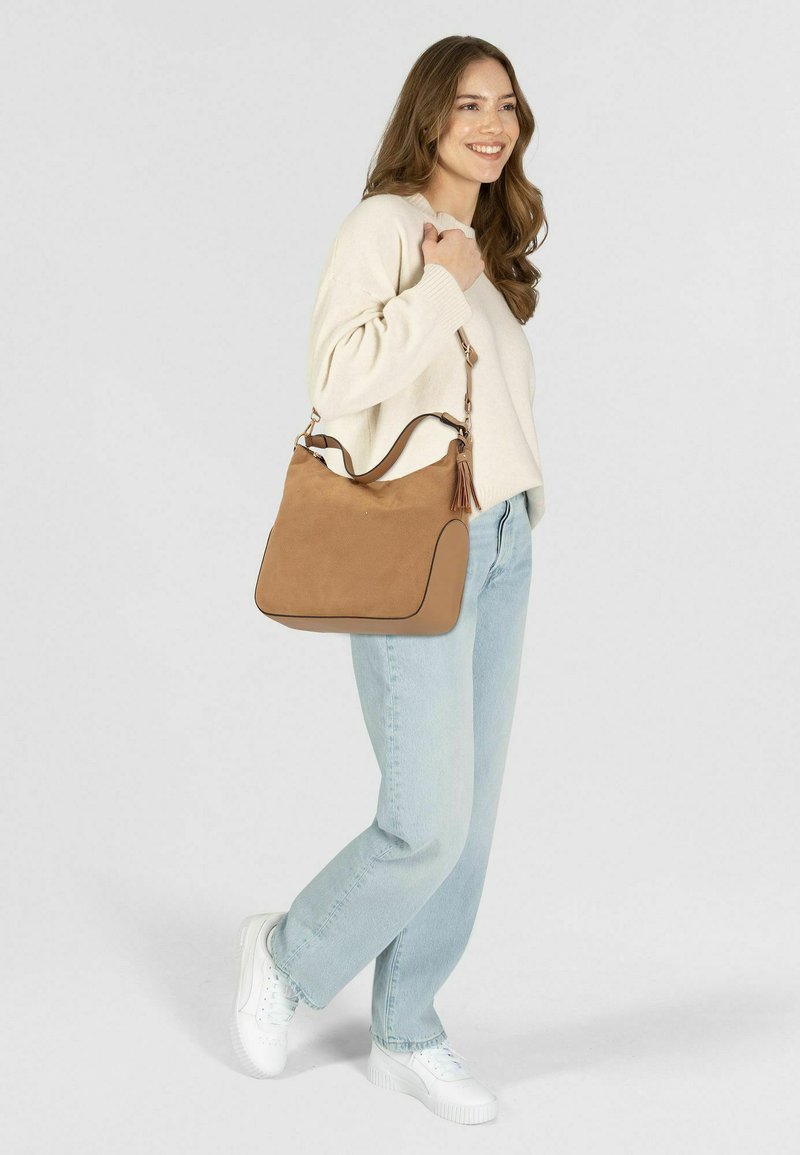 Tasche aus braunem Wildleder mit runder Form, Reißverschluss, Akzentnähten und abnehmbarem Schulterriemen. Sie verfügt über einen dekorativen Quastenanhänger.