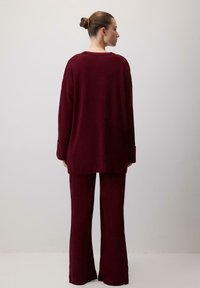 Burgundowa, prążkowana, oversize sweter zestawiony z dopasowanymi spodniami z szerokimi nogawkami, z długimi rękawami i luźnym krojem.