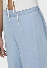 Pantalones de pierna ancha azul claro, hechos de una tela suave, con una textura lisa y una cinturilla elástica con detalles de cordón.