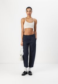Navyblauwe cropped broek met een relaxte pasvorm, voorzien van zakken en een knoopsluiting. Gekleed met een beige crop top en zwarte loafers.