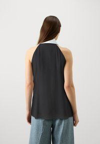 Black halter top with a white collar, made of a smooth fabric. Features a relaxed fit and a curved hem. Back view shows open design.