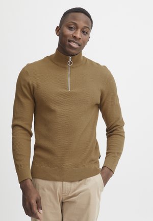 Brown textured turtleneck sweater featuring a half zipper and ribbed cuffs. Paired with light-colored trousers for a casual look.