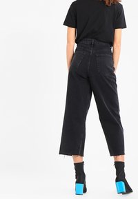 Svarta högmidjade cropped jeans med en avslappnad passform, med fem fickor och rå fåll. I kombination med en svart topp och blå blockklackstövlar.