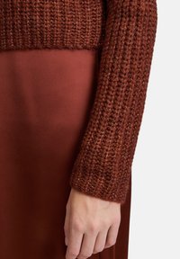Maglione lavorato a maglia di colore ruggine, con una texture a coste, abbinato a una gonna in satin liscia di una tonalità simile.